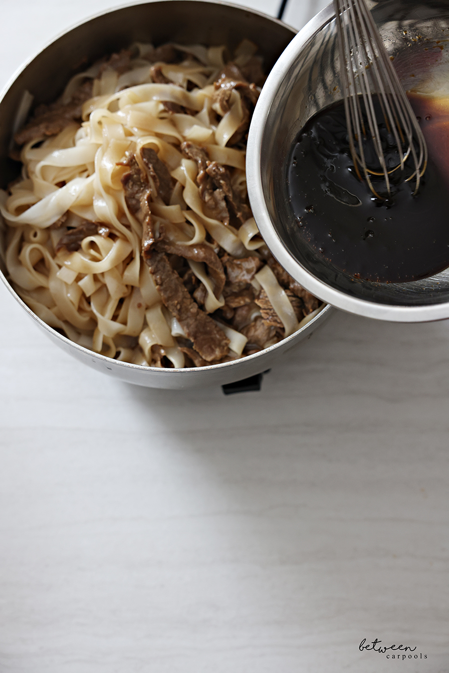 Adding stir-fry sauce to cooked Wide Rice Noodles and steak in a large pan.