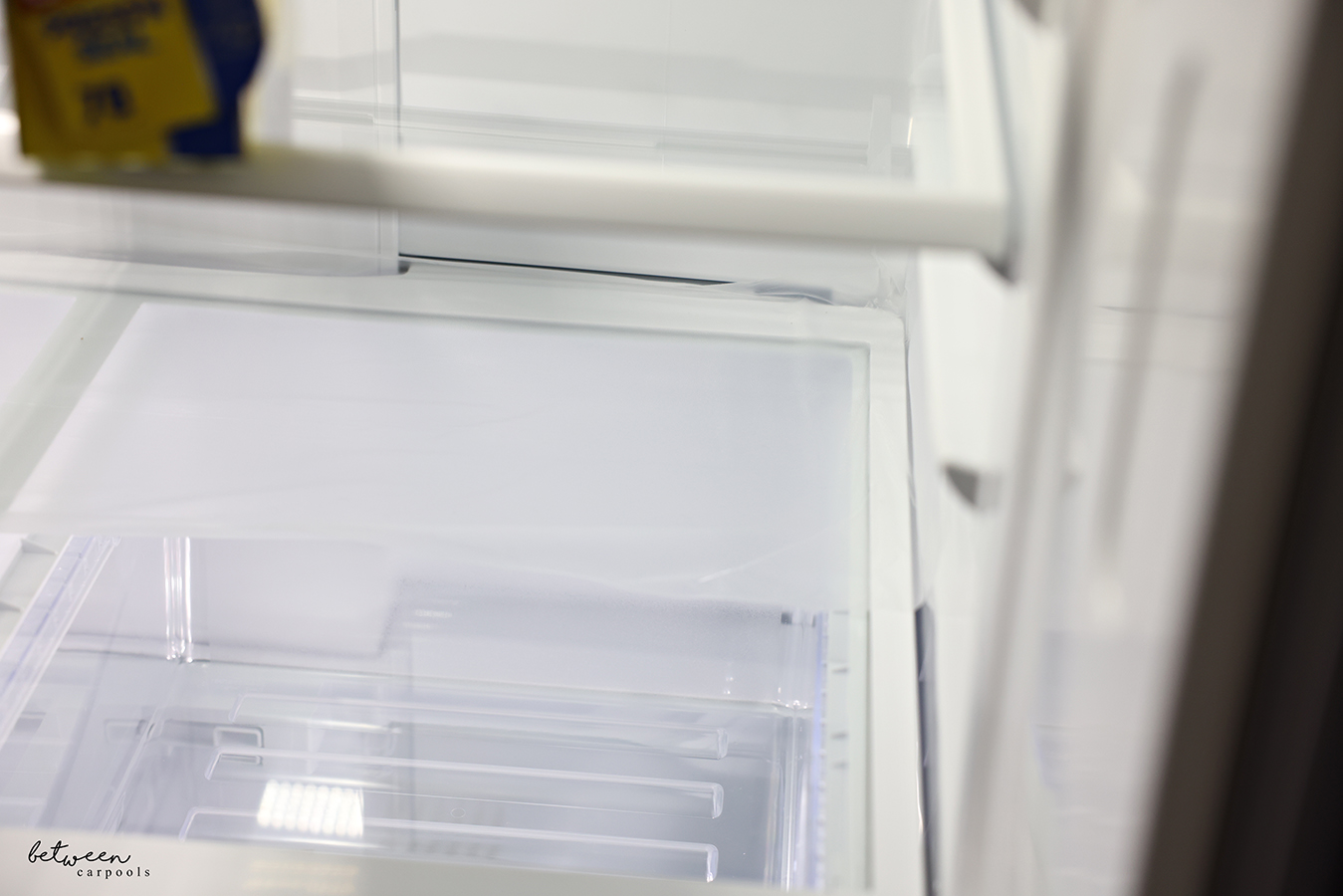 Glad Press n' Seal pressed down on the plastic frame of a clean fridge shelf.