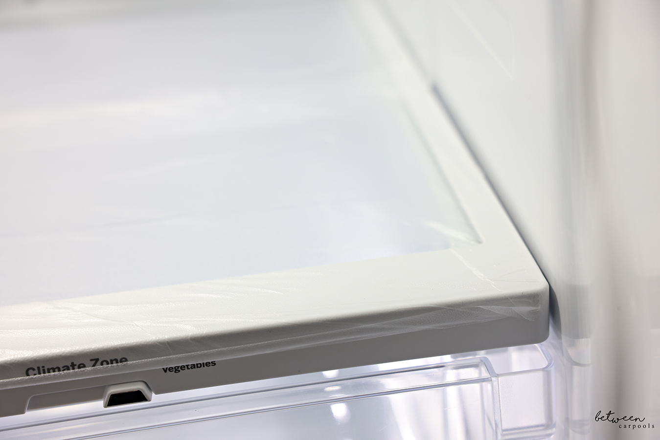 Closer view of Glad Press n' Seal pressed down on the plastic frame of a clean fridge shelf.