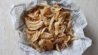 Fried onion strings in a newspaper parchment lined bowl.