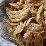 Closeup of Fried onion strings in a newspaper parchment lined bowl.
