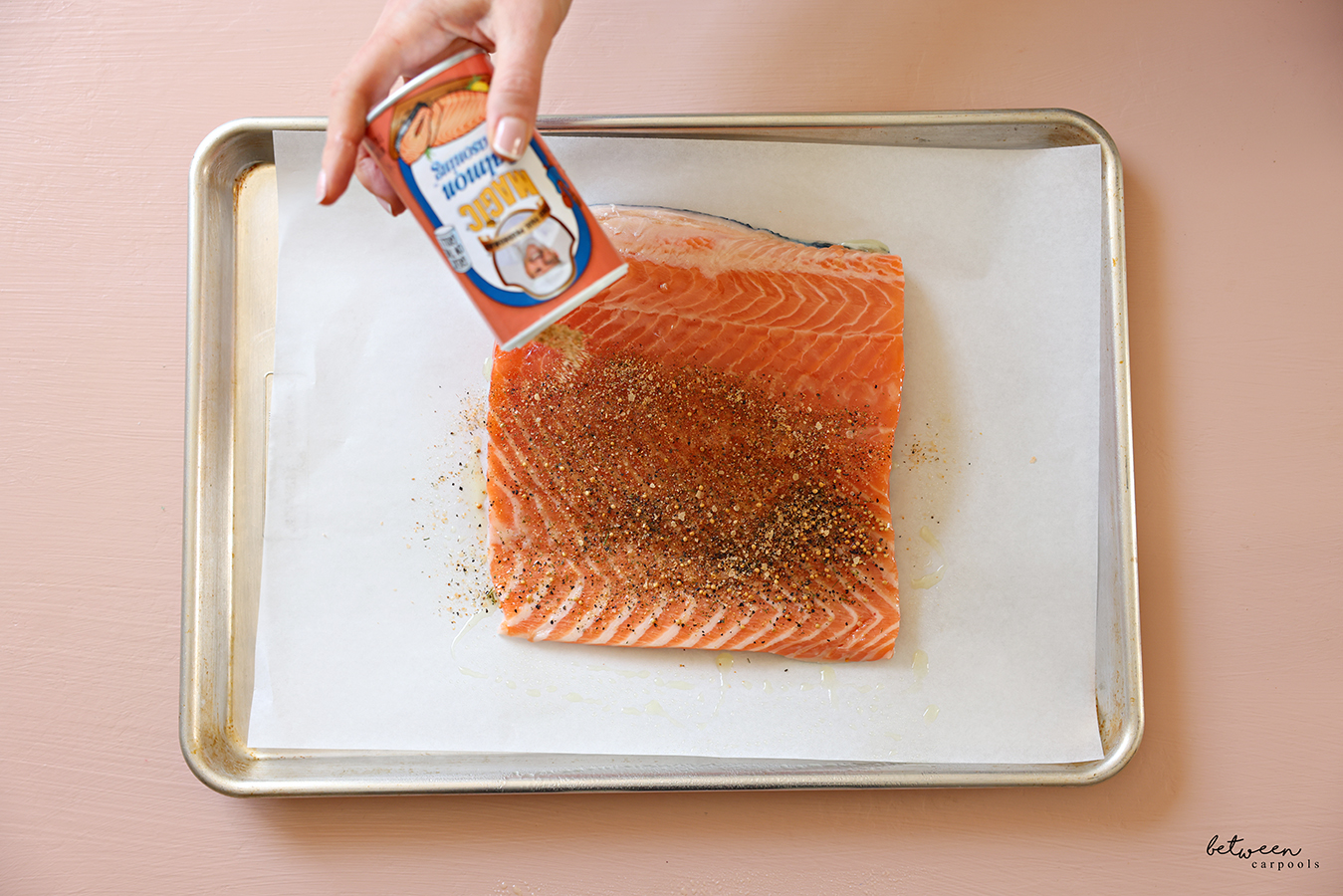 Sprinkling Magic Salmon Seasoning over oiled salmon on a parchment lined baking sheet.