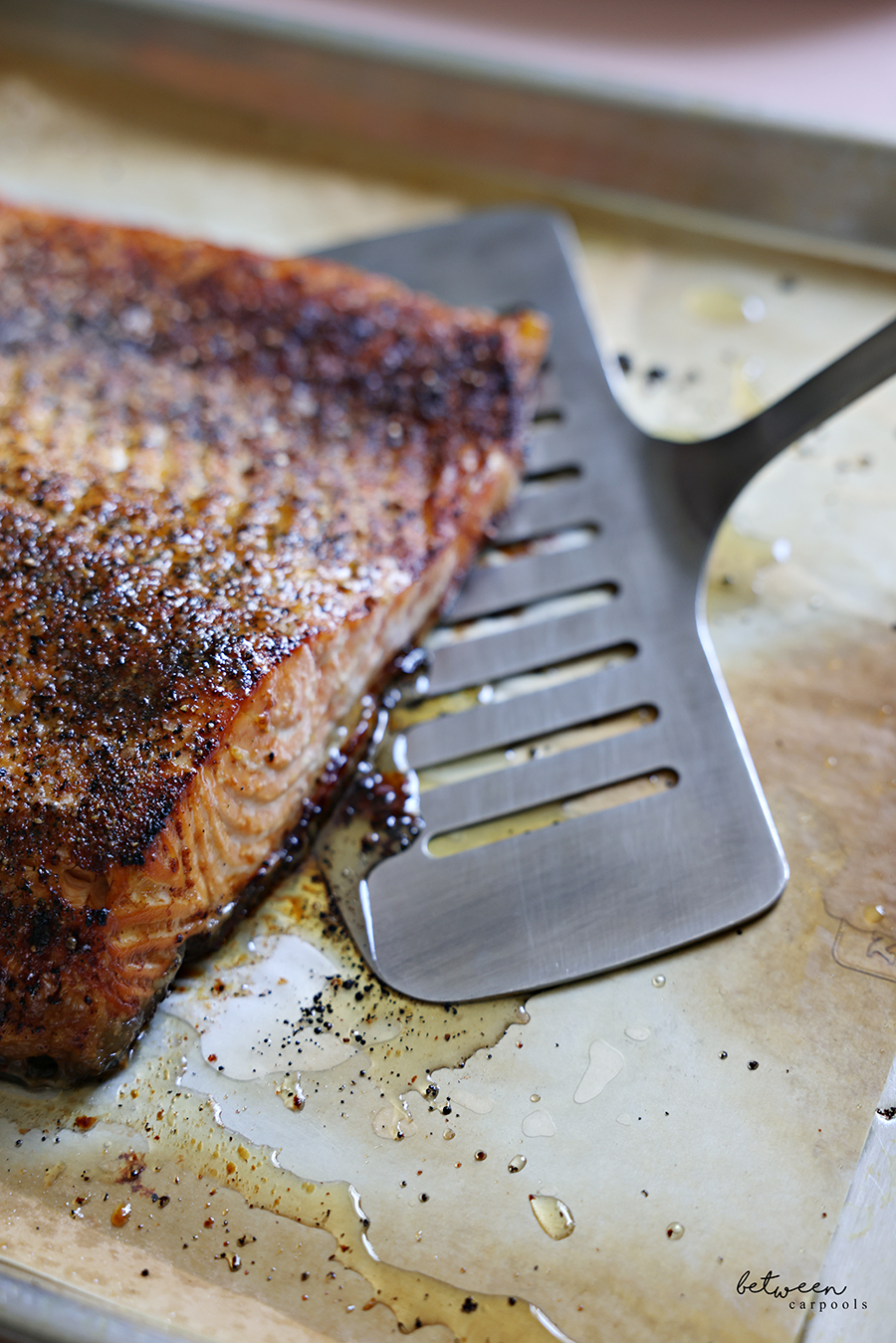 Removing baked salmon from parchment lined baking sheet with a fish spatula.
