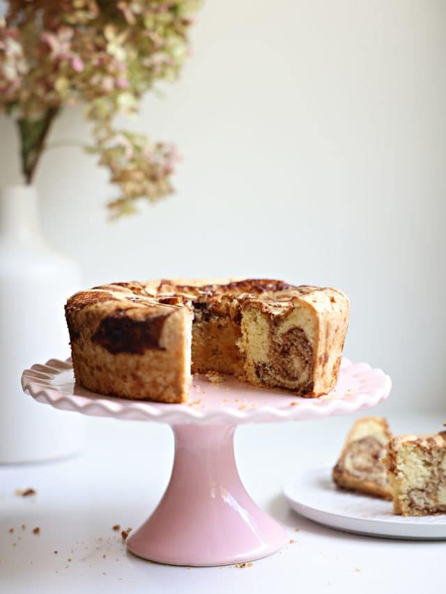 Marble cake on a pink scalloped cake stand. Slices from the cake on a plate nearby.