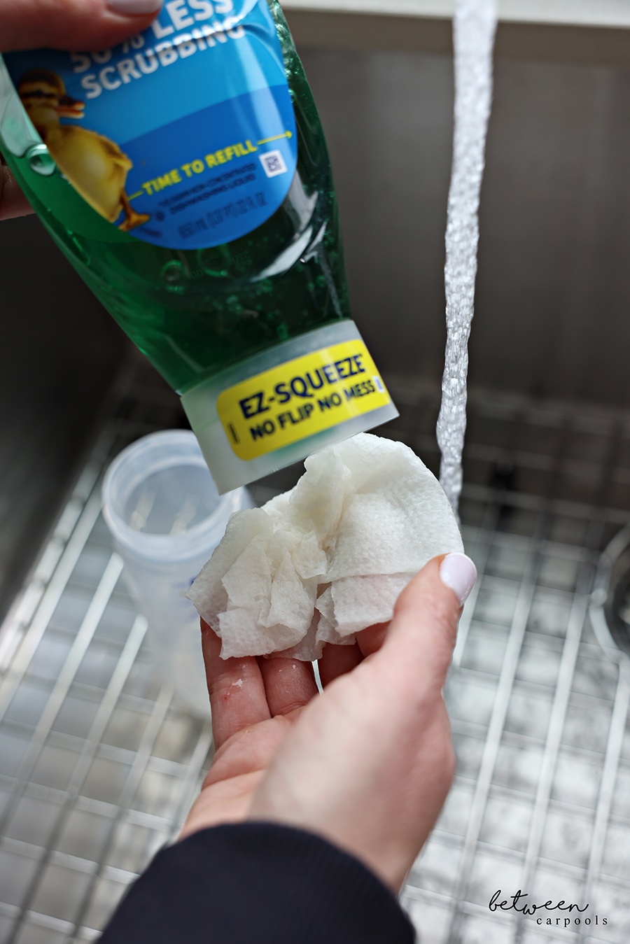 Adding dish soap to a very wet paper towel over the kitchen sink.