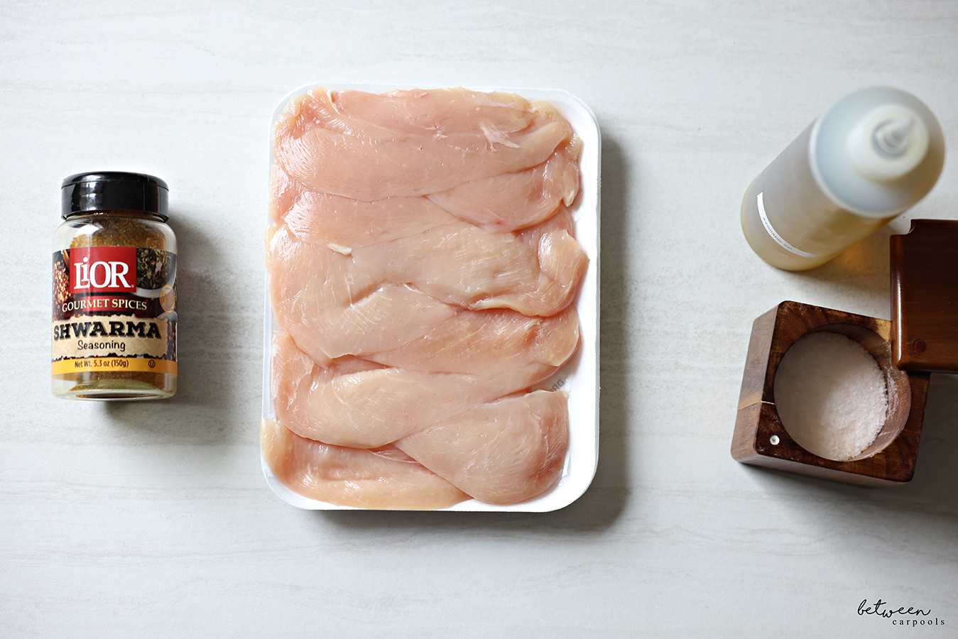 Top view of LiOR Shwwarma Seasoning, a package of thin chicken cutlets, avocado oil and an open salt cellar.