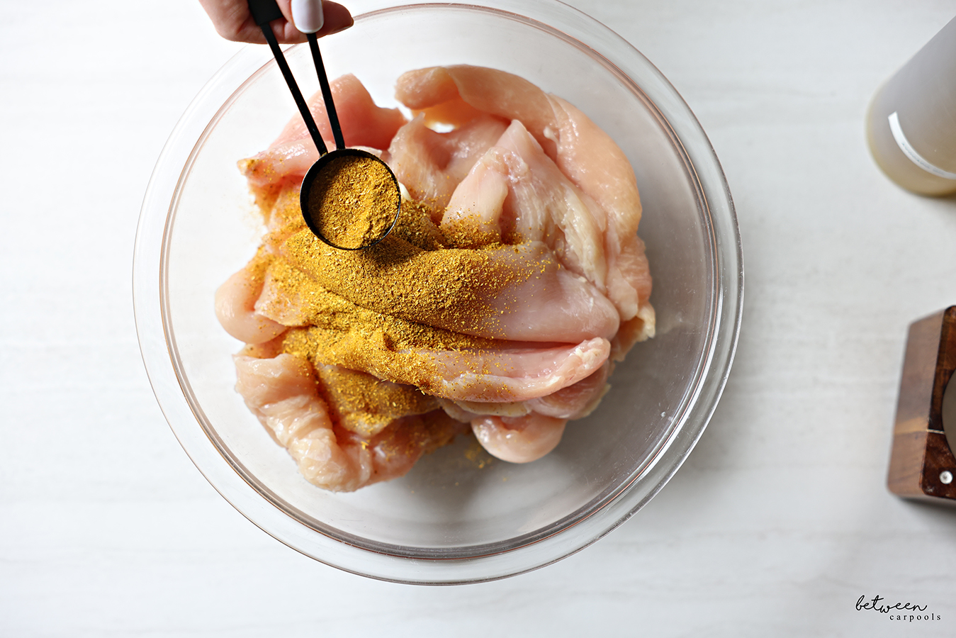 Adding shwarma spice mix to thin cutlets in a glass mixing bowl.