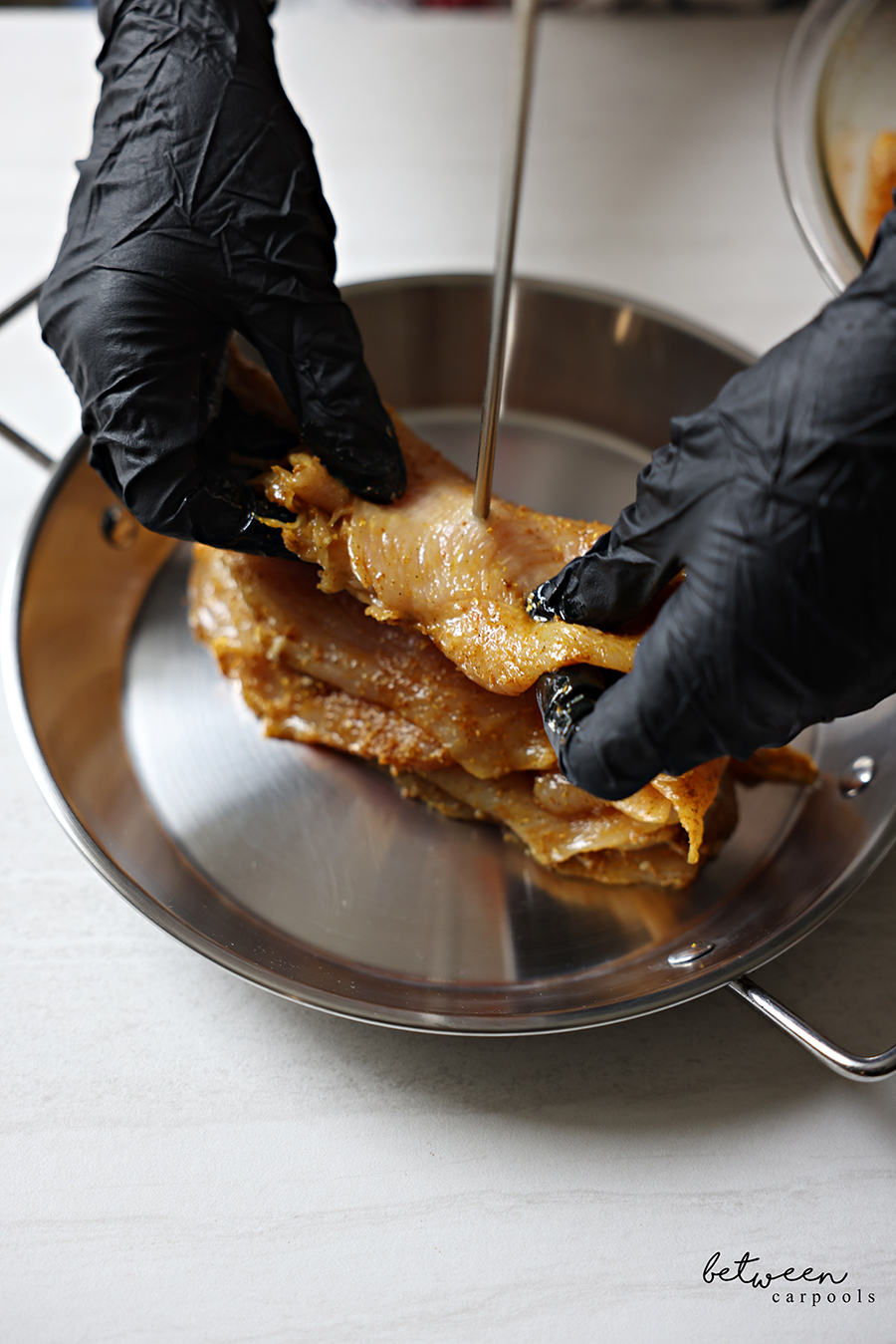Layering seasoned chicken cutlets by poking them through the center of an Al Pastor Vertical Skewer.