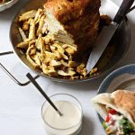 Sliced shawarma chicken off the skewer in an Al Pastor Vertical Skewer, a bowl of salad, a glass of techina, and a pita with those components plated.