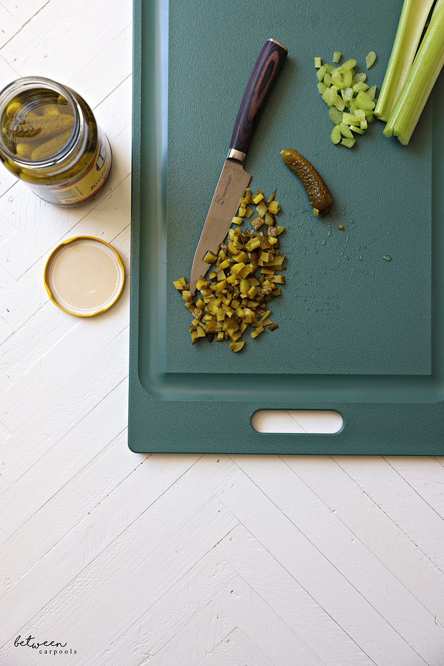 Top View of a plastic cutting board with whole and diced celery and gherkn pickles, and an open jar of B&G Kosher Baby Dill Gherkins nearby.