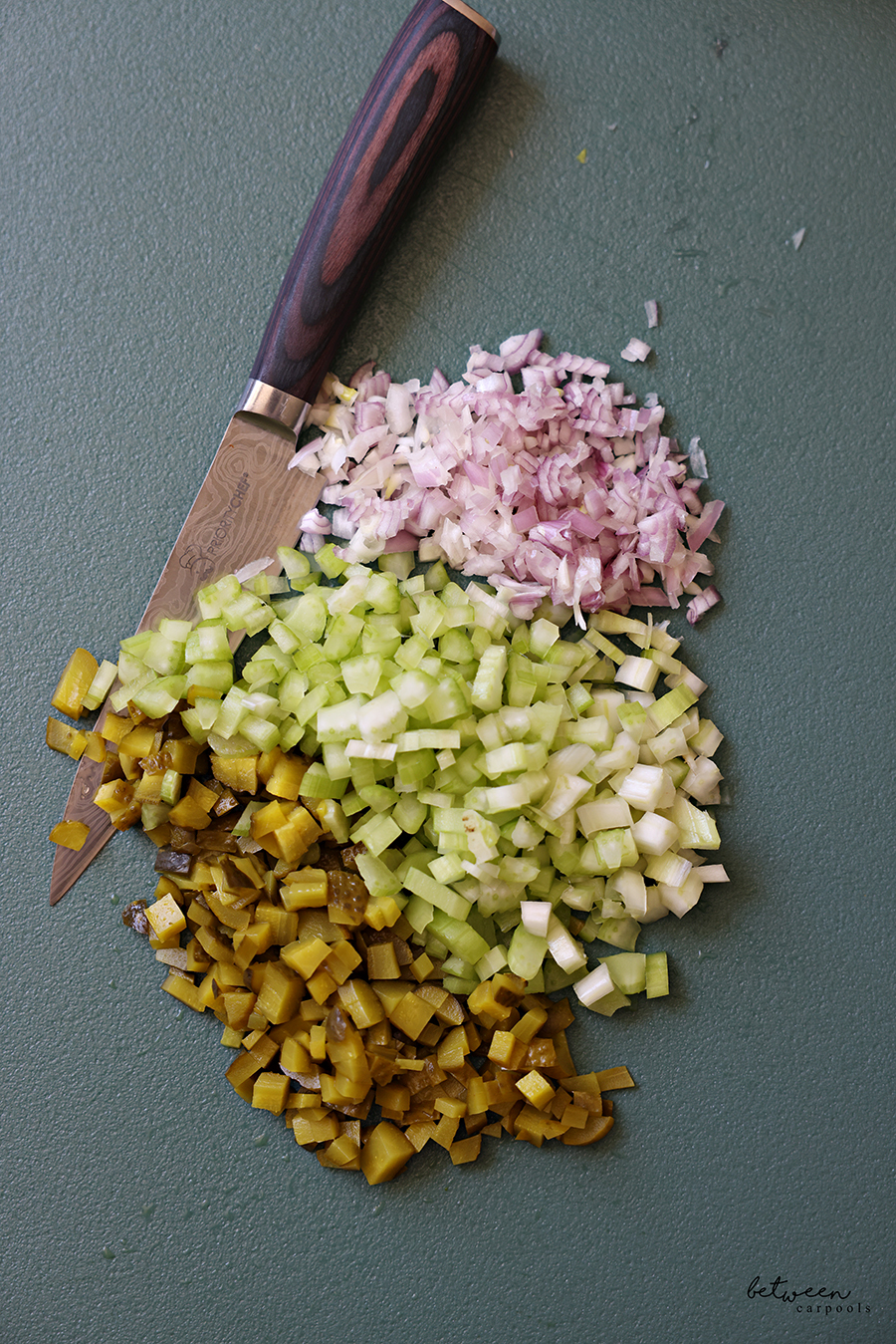 Finely diced gherkin pickles celery and shallot on a plastic cutting board.
