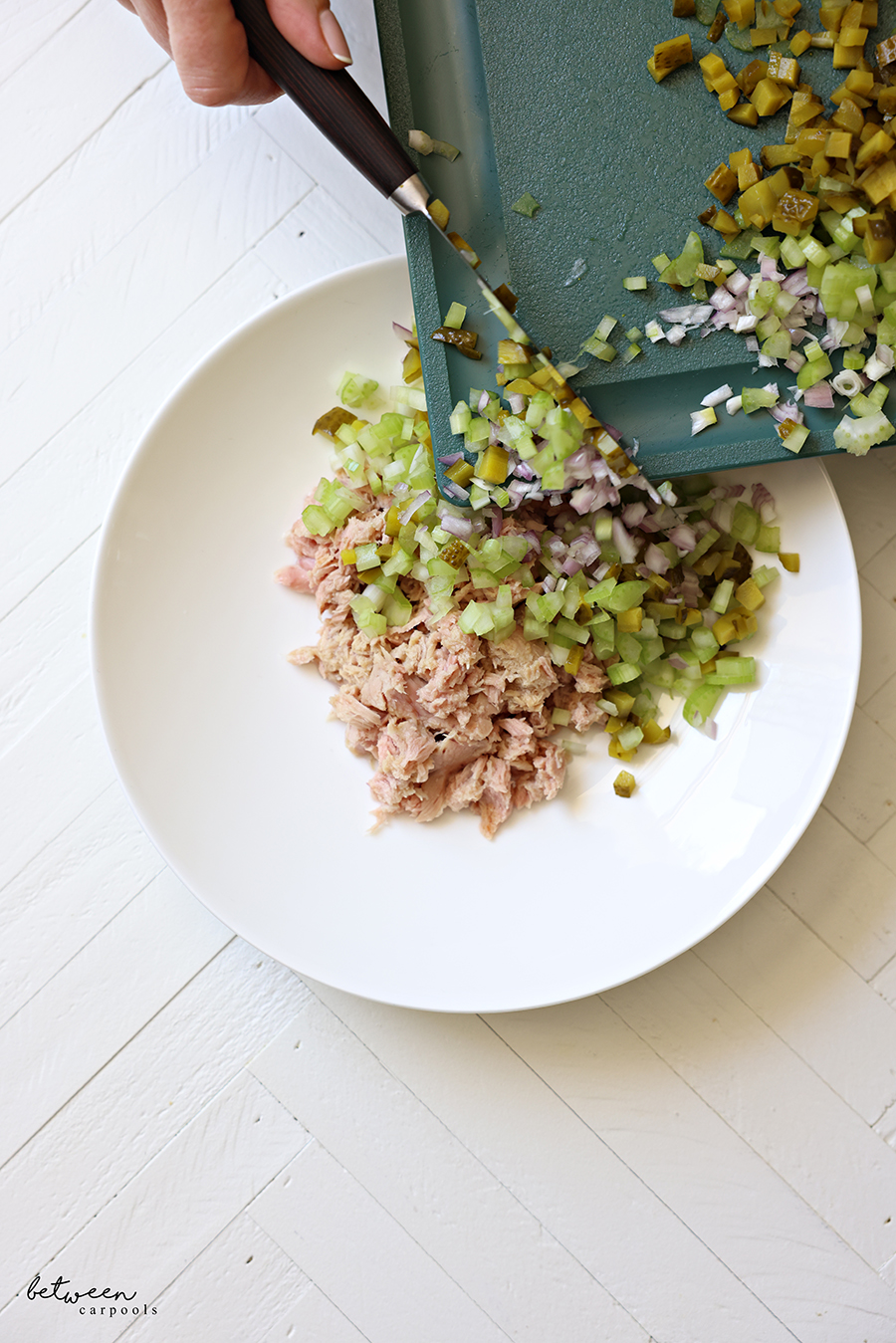 Adding finely diced gherkin pickles celery and shallot into a bowl with drained tuna from cans.