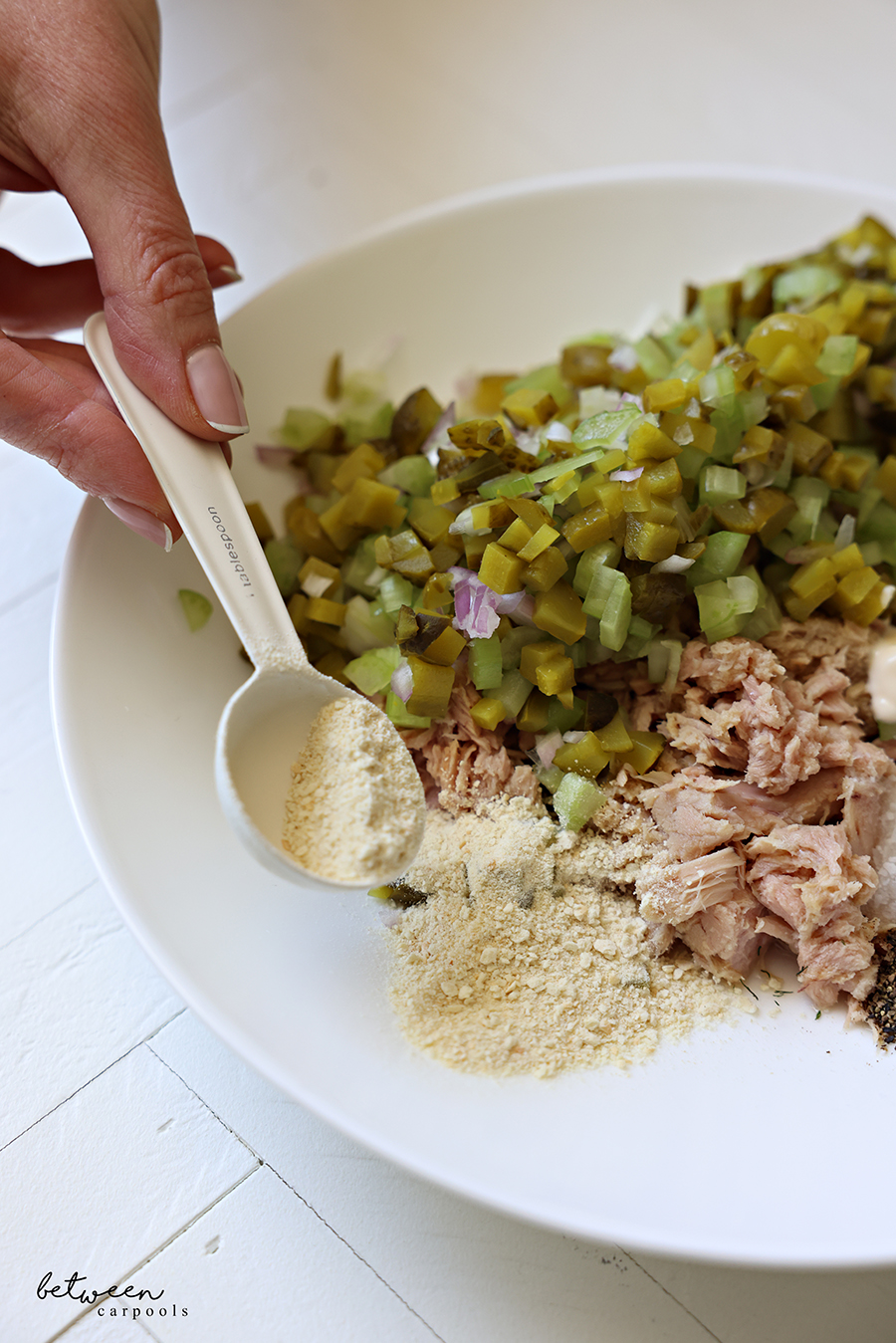 Adding plain breadcrumbs to the side of a bowl with tuna, diced gherkin pickles celery and shallot.
