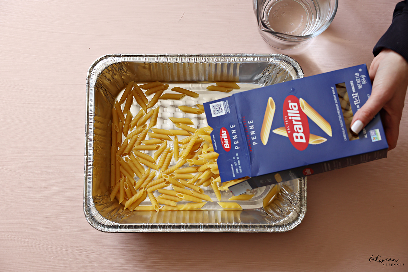 Adding penne pasta to a 9x13-inch aluminum foil pan.
