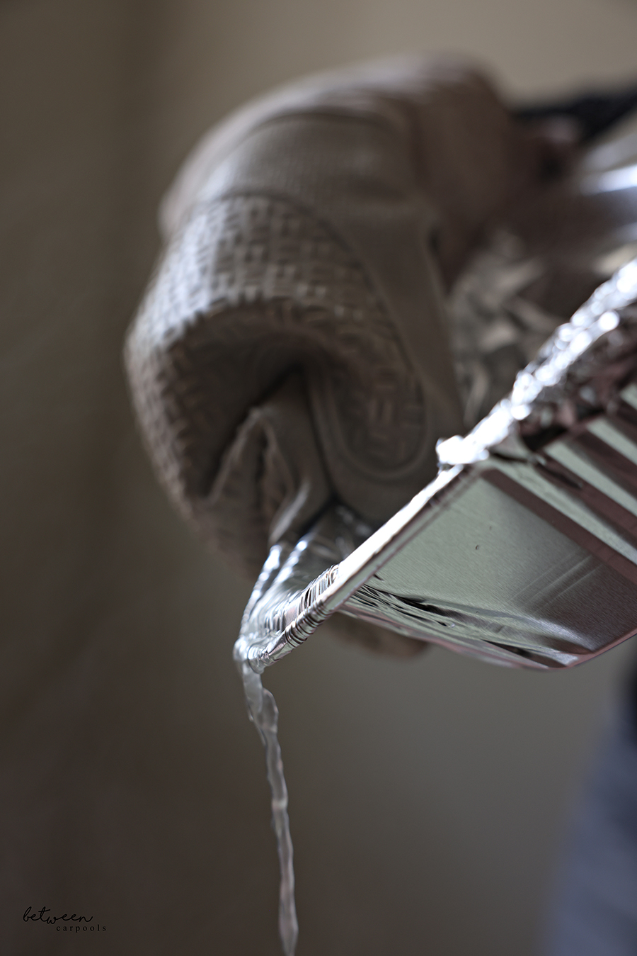 Using its foil cover and a towel, draining pasta water from a 9x13-inch aluminum foil pan into the kitchen sink.