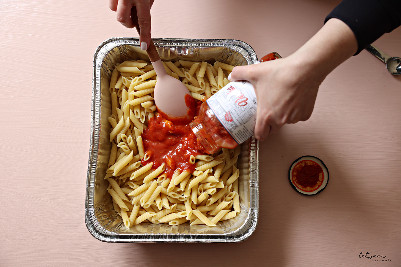 Adding marinara sauce to cooked pasta in a 9x13-inch aluminum foil pan.