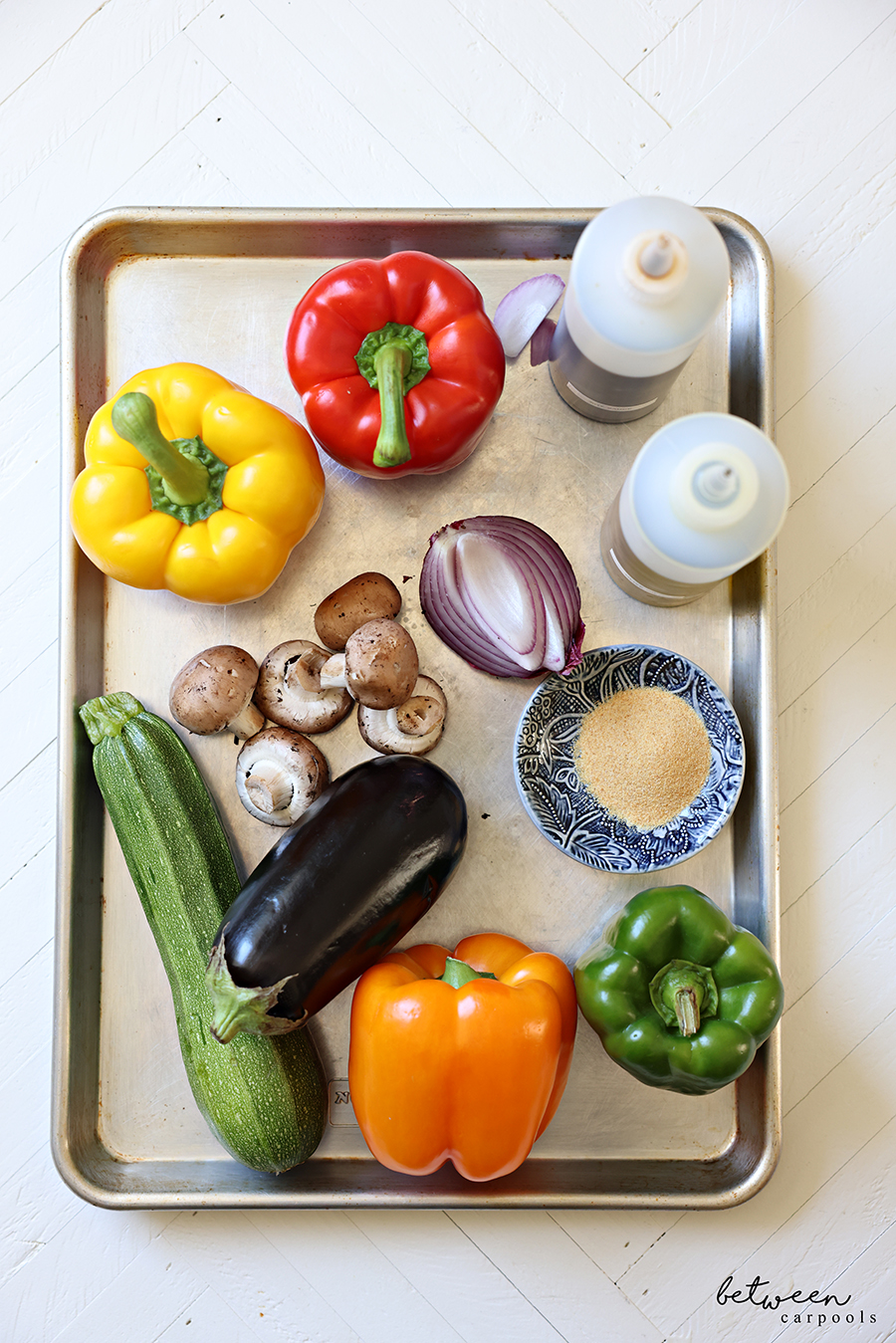 Peppers, red onion, mushrooms, eggplant, zucchini, garlic powder and squeeze bottles of olive oil and soy sauce, on a metal baking sheet.