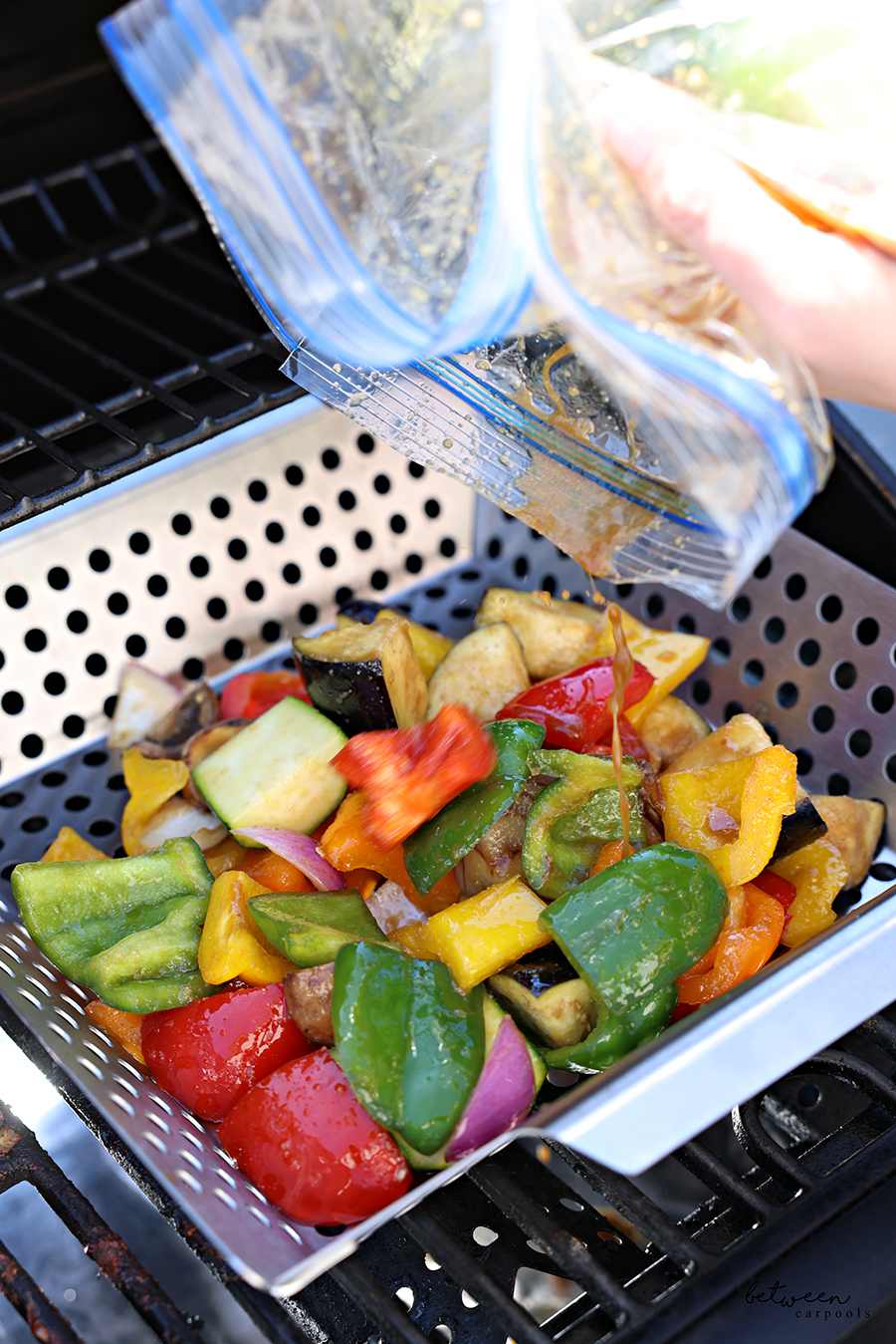 Pouring marinade from the Ziploc onto large diced + marinated vegetables in a grill basket on the grill.
