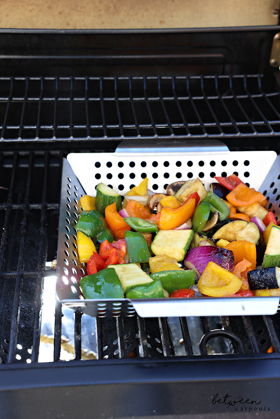 Large diced + marinated vegetables in a grill basket on the grill.
