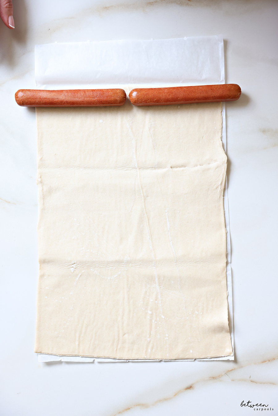 Two hot dogs placed along the short edge of a sheet of puff pastry.