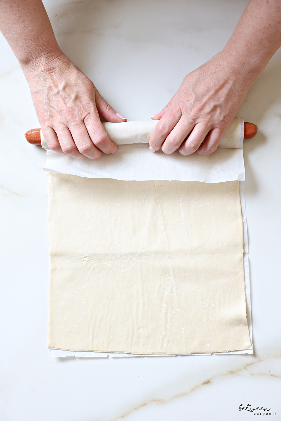 Rolling puff pastry tightly around two hot dogs placed along the short edge of a sheet of pastry.