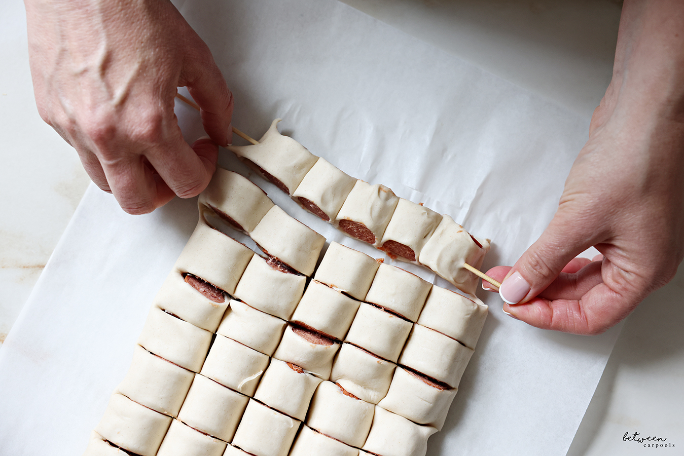 Threading hot dogs wrapped in puff pastry through a long skewer for Puff Pastry Hot Dogs on a Stick.
