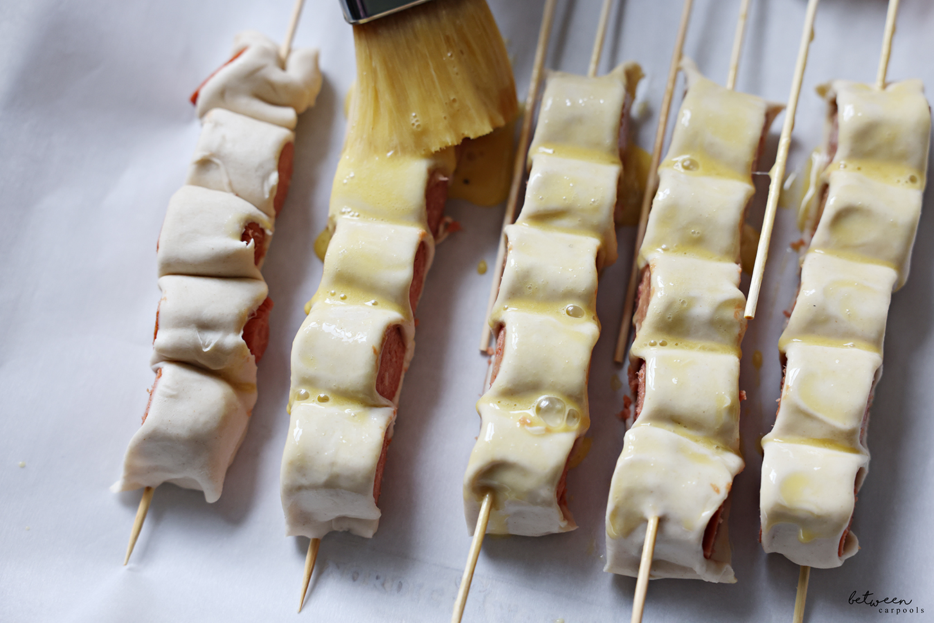Brushing egg on Puff Pastry Hot Dogs on a Stick.