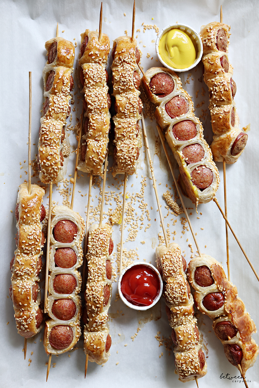 Baked Puff Pastry Hot Dogs on Sticks with portion cups of ketchup and mustard.