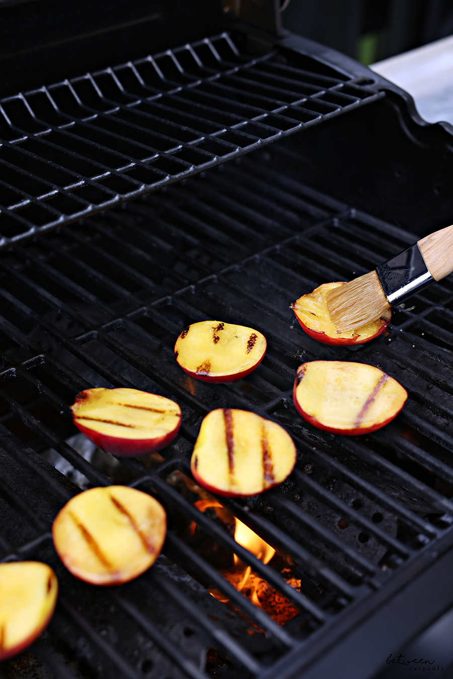 Brushing bourbon glaze on halved peaches on the grill.