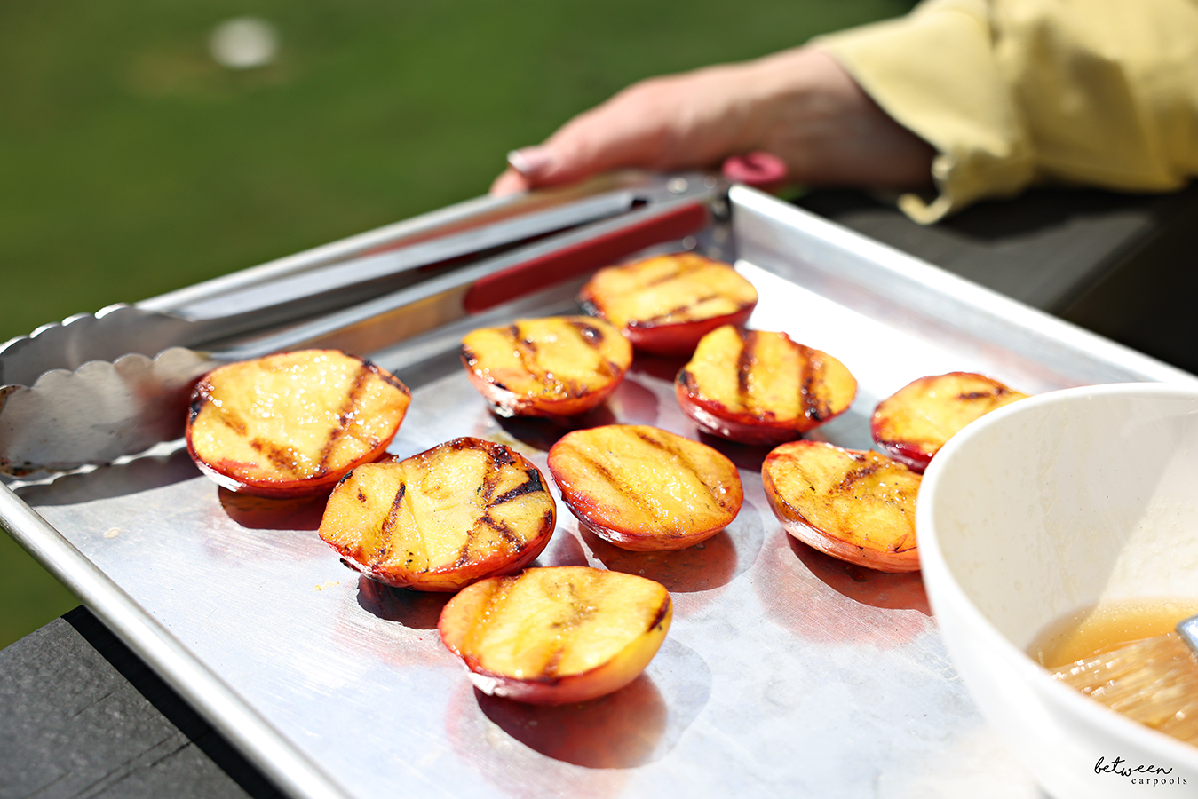 Holding a metal sheet pan with grilled peaches and bourbon glaze. Beautiful image! Gorgeous day!