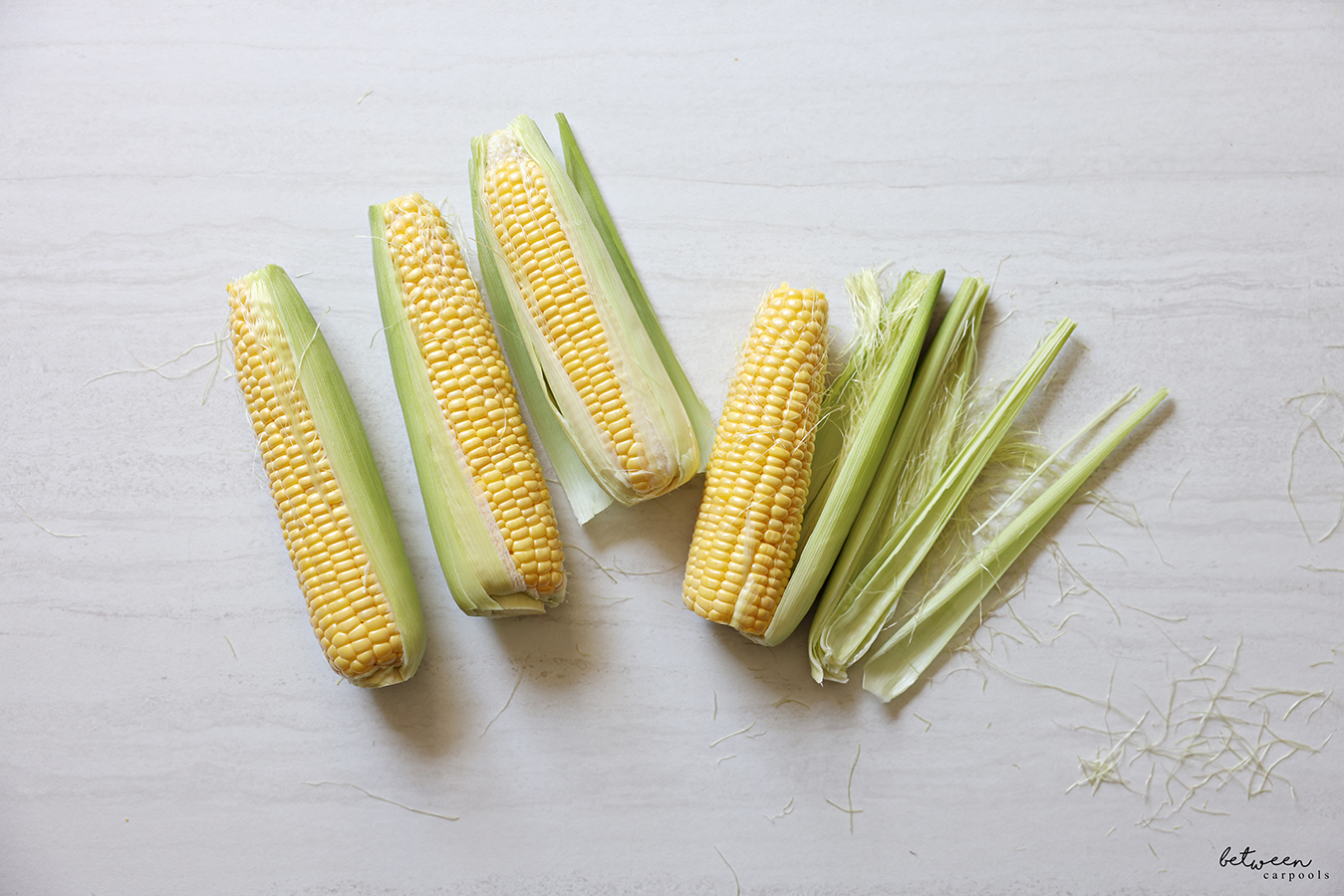 Four ears of fresh corn; tips and stalk ends cut and partial husks removed.