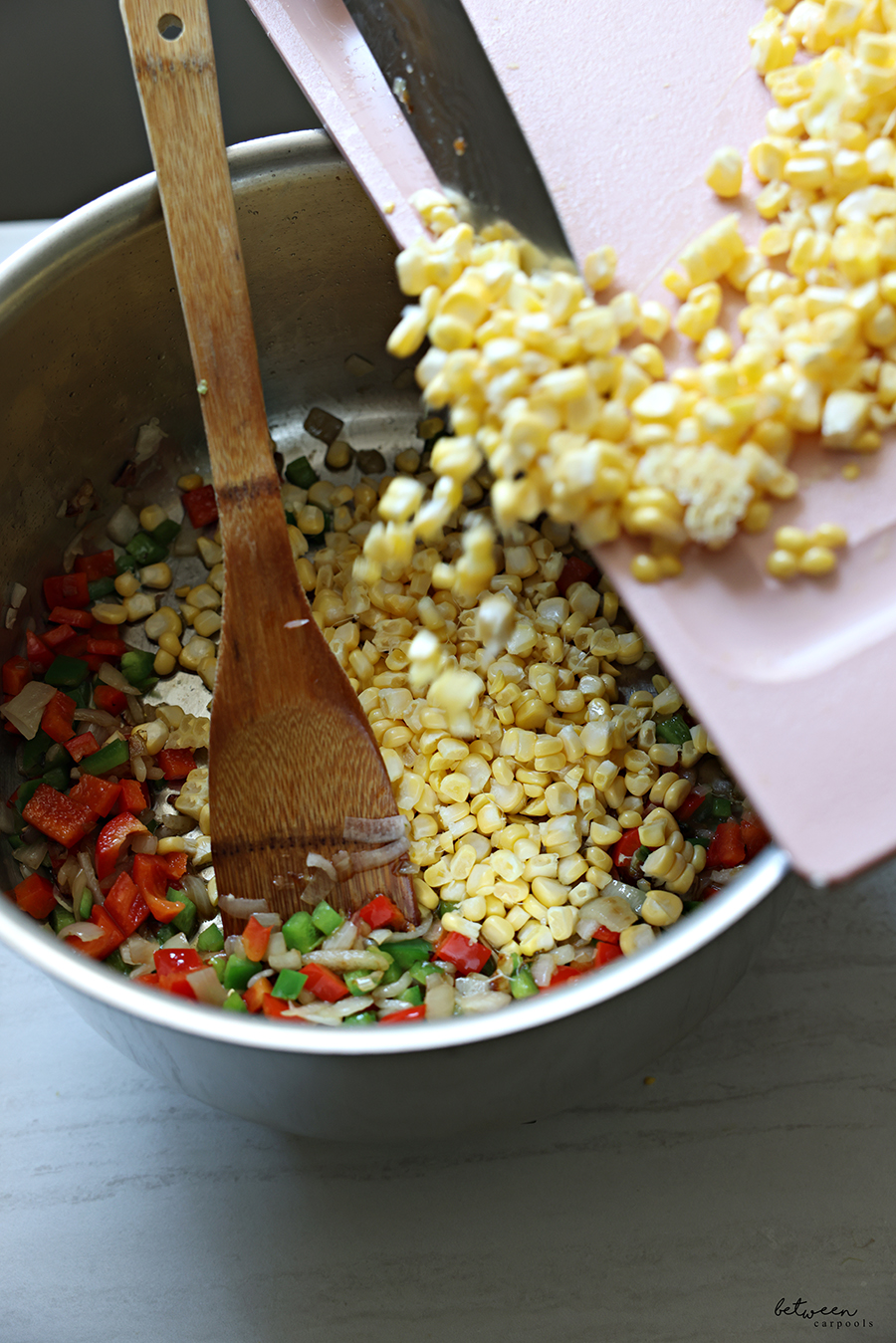 Adding fresh corn kernels to a sauté pan with diced shallot, jalapẽno and red bell pepper.