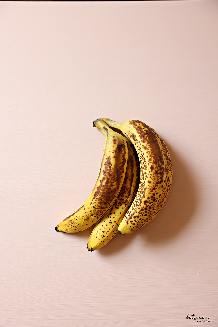 3 overripe bananas on pink.