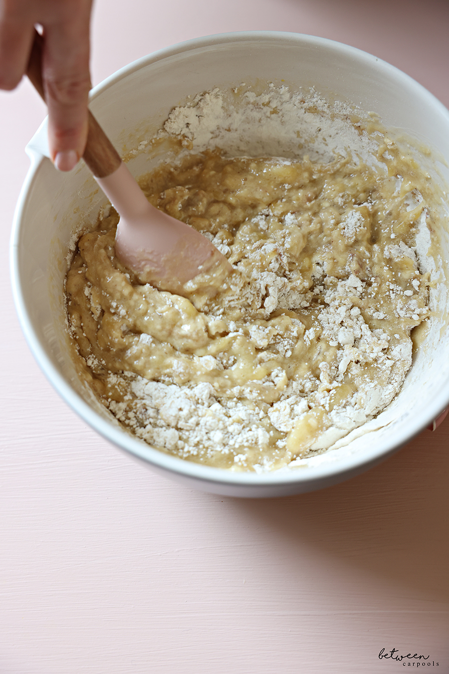Mixing all ingredients for banana muffins in a mixing bowl with a spatula.