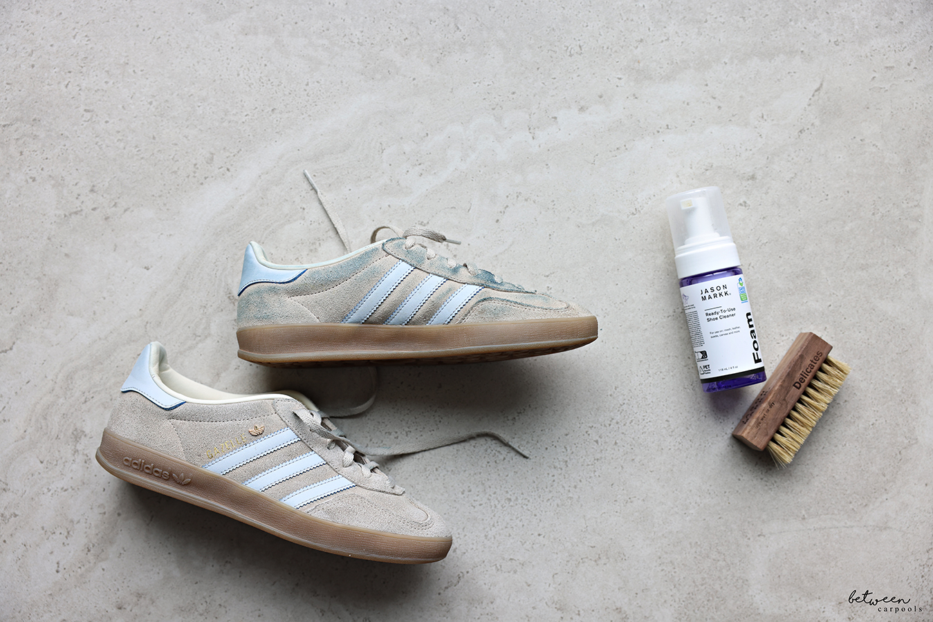 Jason Markk foaming cleaner and soft bristle brush near a pair of adidas GAZELLE sneakers.