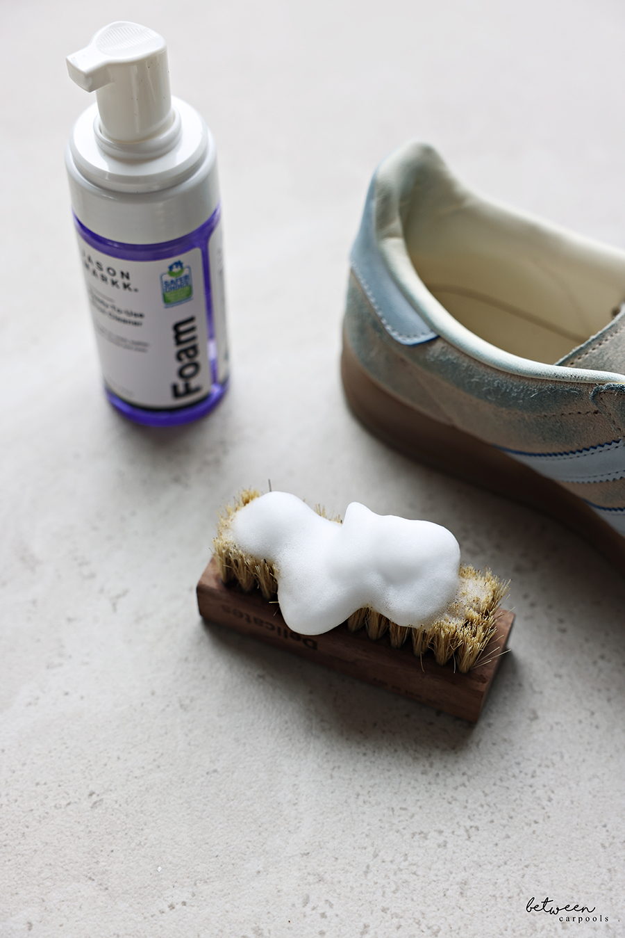 Closeup of Jason Markk foaming cleaner on a soft bristle brush near an adidas GAZELLE sneaker.