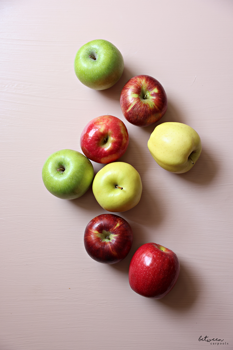 A variety of apples on pink background.