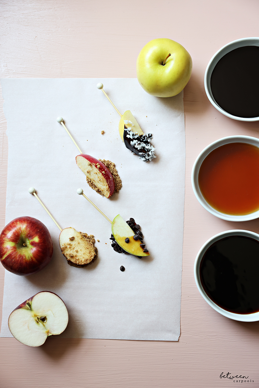 Skewered apple spears, dipped and topped, on parchment paper.