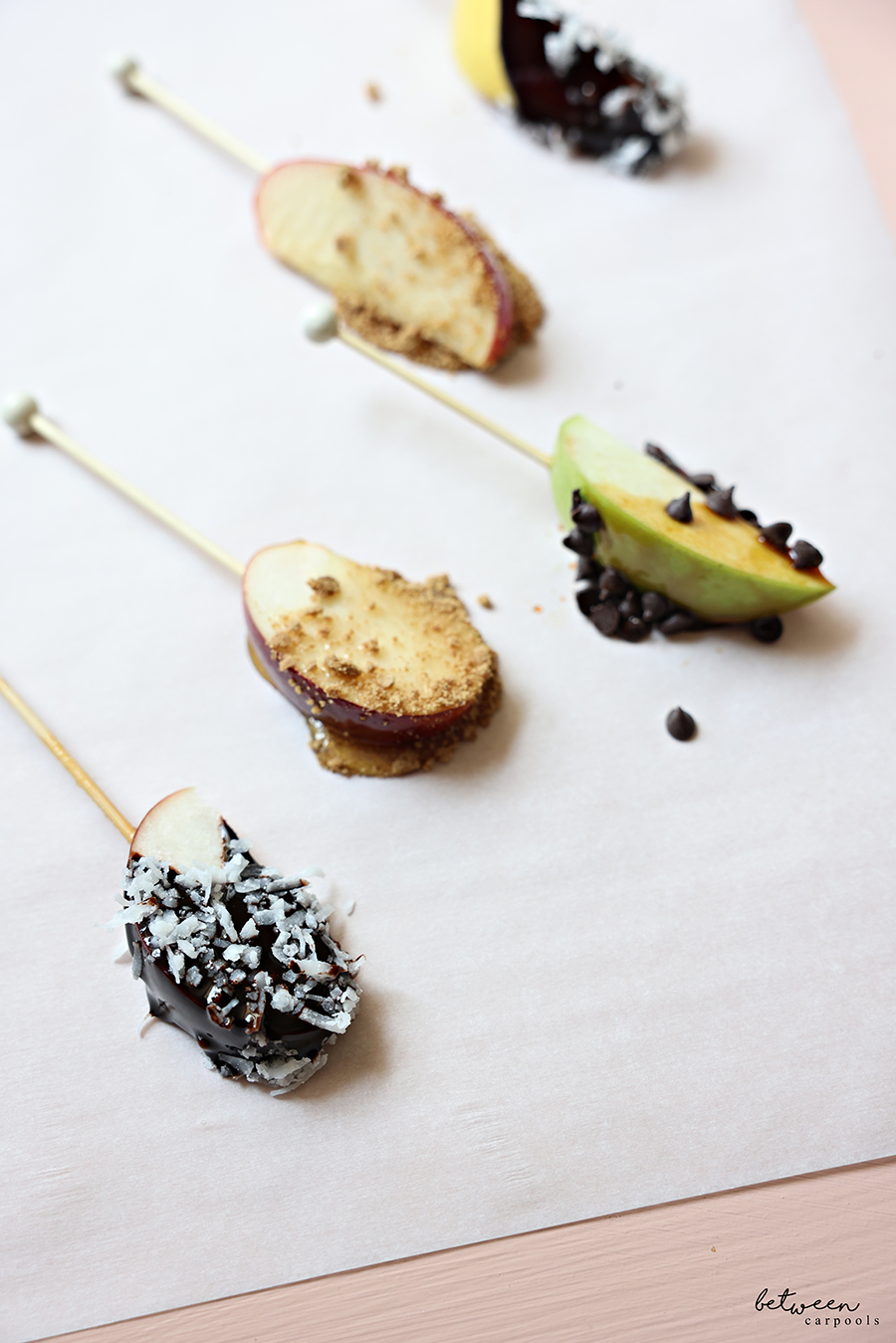 Closeup of skewered apple spears, dipped and topped, on parchment paper.