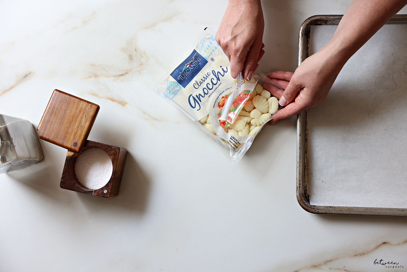 Opening a package of Tuscanini Classic Gnocchi. Black pepper, an open salt cellar and a parchment lined baking sheet nearby.