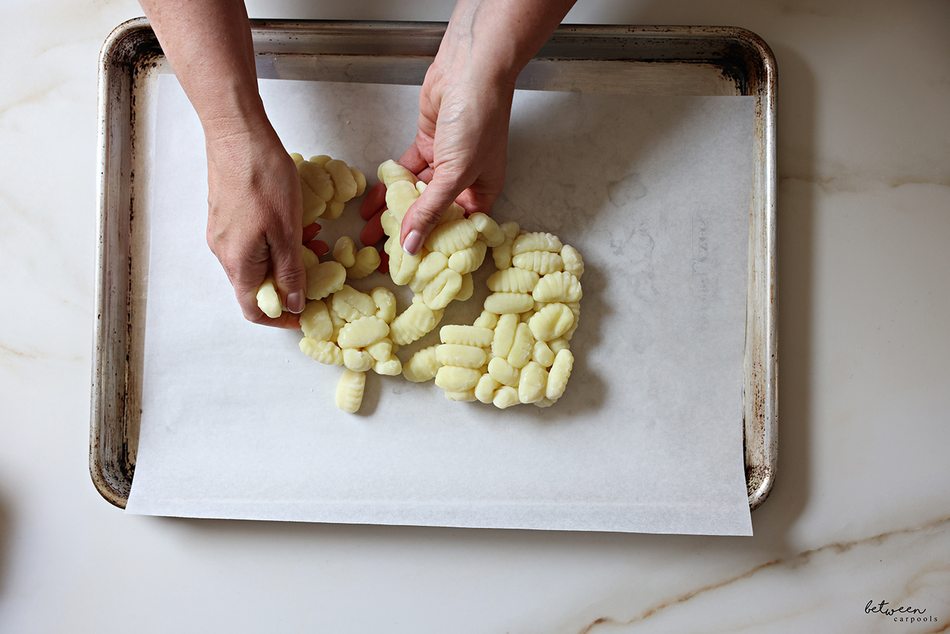 Carefully peeling individual pieces of gnocchi apart on a parchment lined baking sheet.