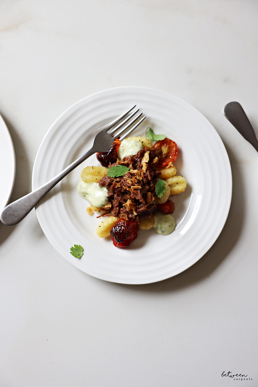 Plated gnocchi with shredded beef, garnished with crispy onions, garlic parsley sauce and fresh parsley.